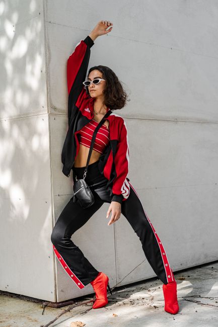Fashionable woman in red and black outfit posing against a white wall.