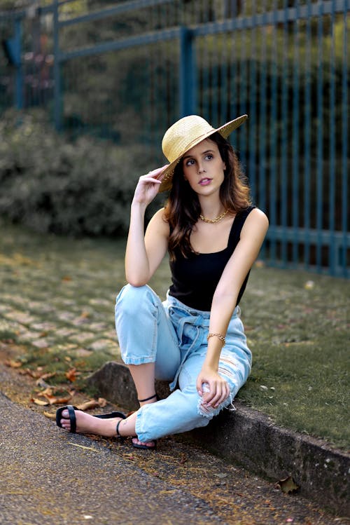 A Beautiful Woman in Black Tank Top and Denim Jeans Sitting on the Street