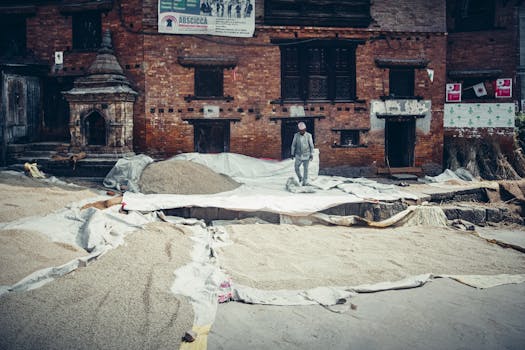 A man drying grains outside a historic brick building, showcasing traditional harvest methods.