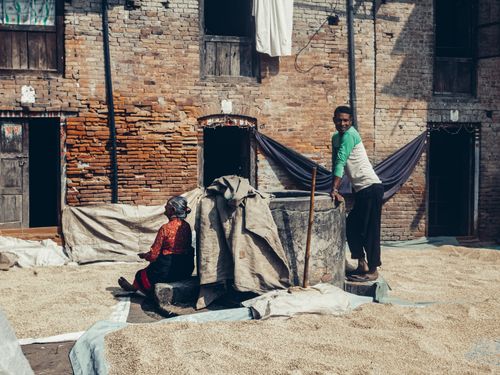 Free A man and a woman work in a rustic courtyard, drying grains under the sun. Stock Photo