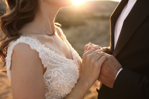 Close-up of bride and groom holding hands during a sunset wedding ceremony.