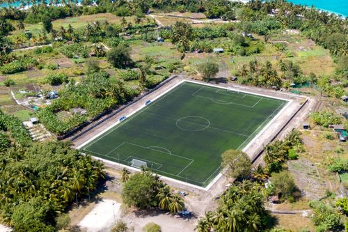Free Aerial view of soccer field surrounded by lush greenery and palm trees in a tropical landscape. Stock Photo