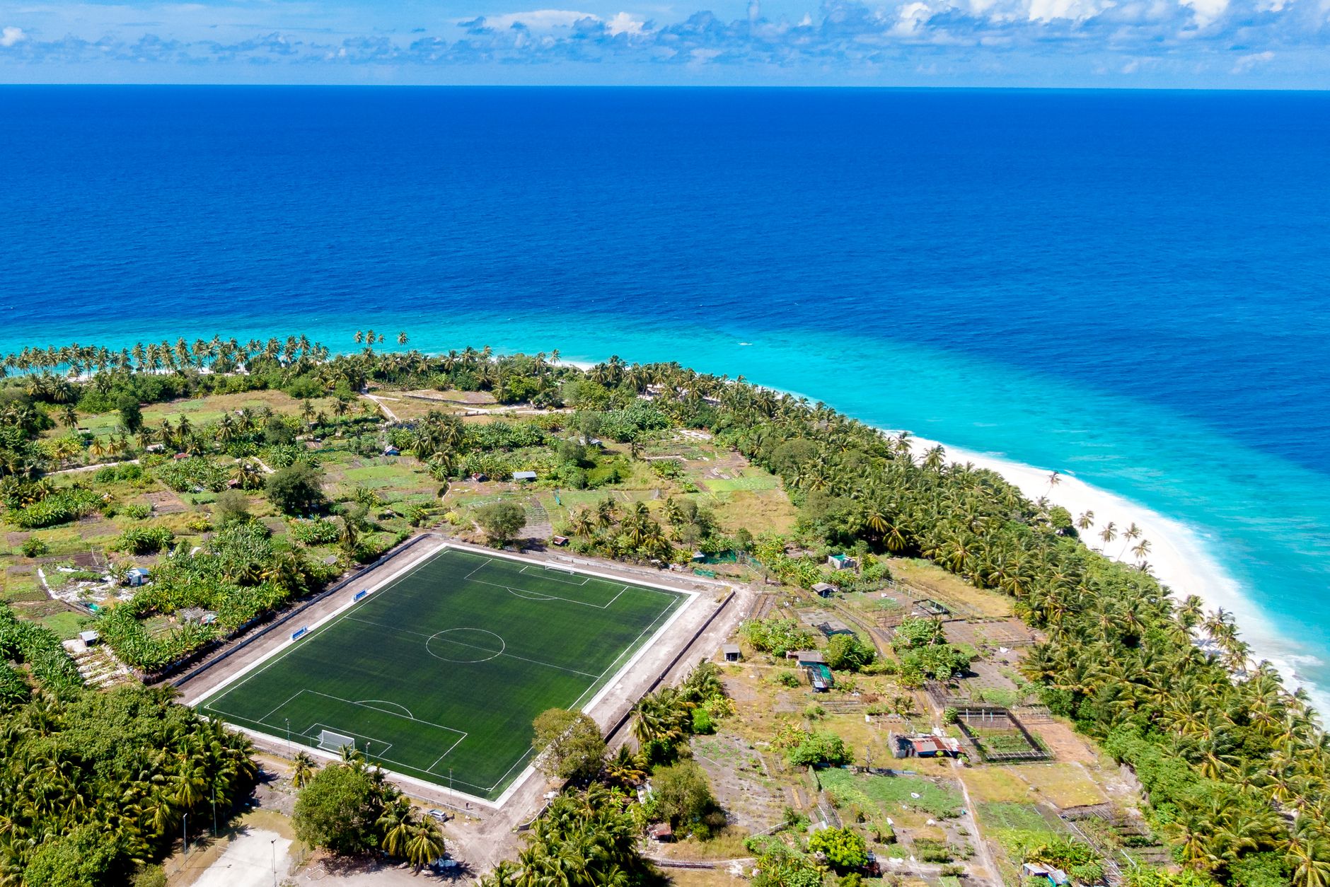 Stunning aerial view of a soccer field on a tropical island by the ocean.