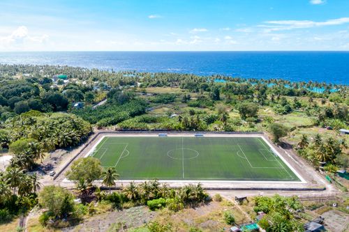 Free Drone shot of a coastal soccer field surrounded by lush greenery and ocean. Stock Photo