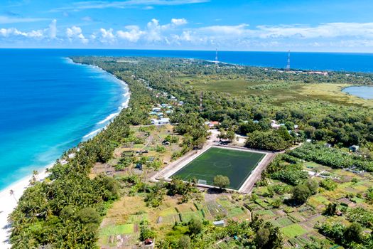 Stunning aerial shot over a tropical coastline with a soccer field nestled among green landscapes.
