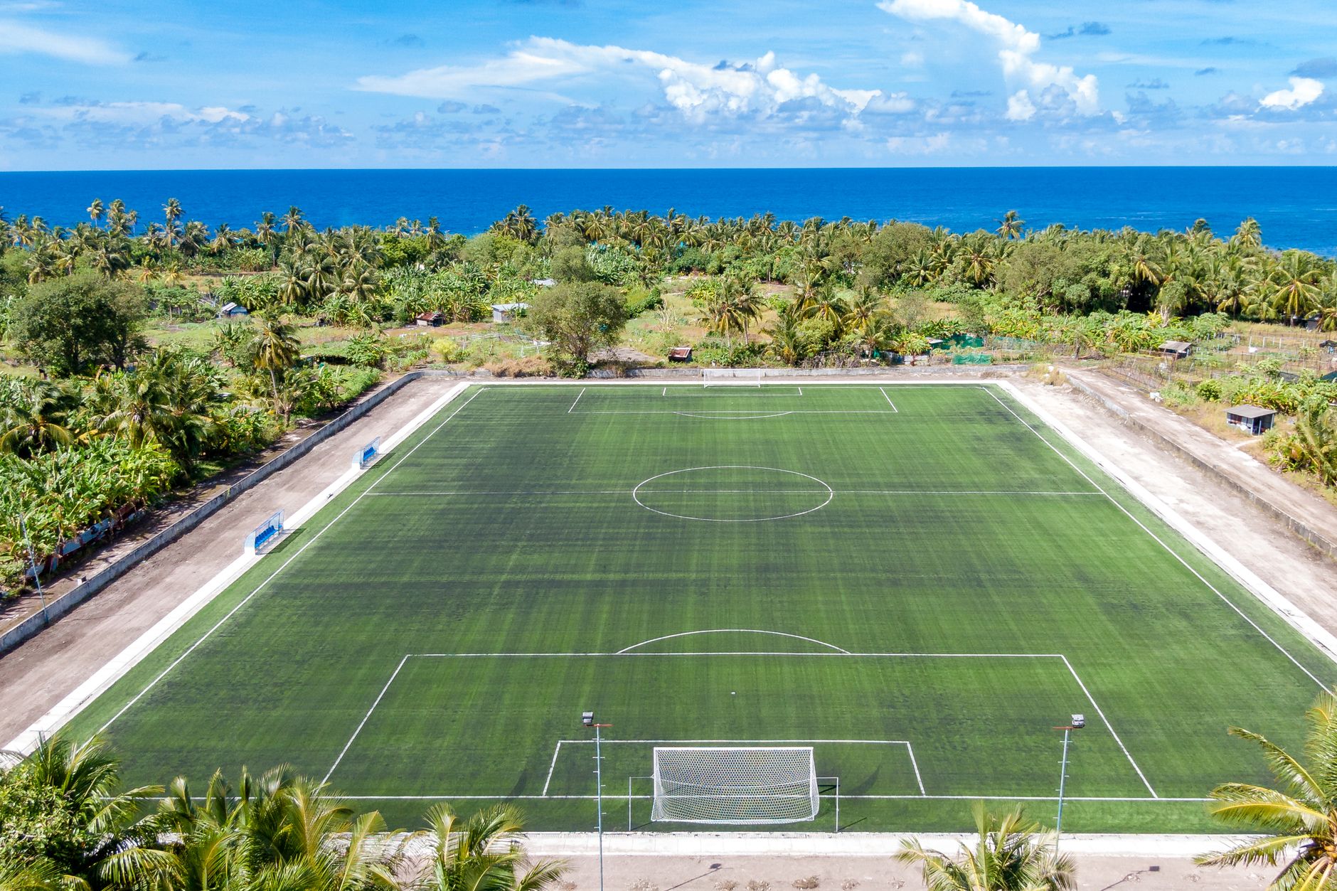 wide football pitch at sunrise with players performing resisted sled sprints beside marked cones