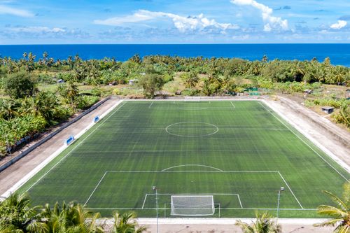 Free Aerial shot of a soccer field by the ocean, surrounded by lush tropical plants and blue skies. Stock Photo