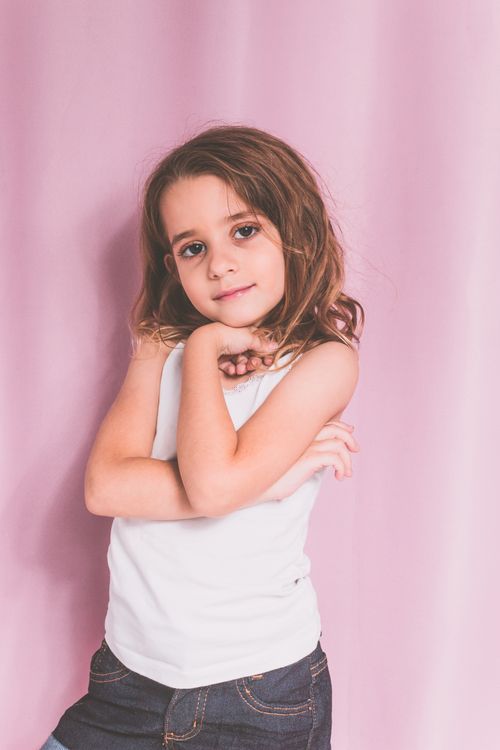 Free Charming young girl in casual outfit posing confidently against a pink backdrop. Stock Photo