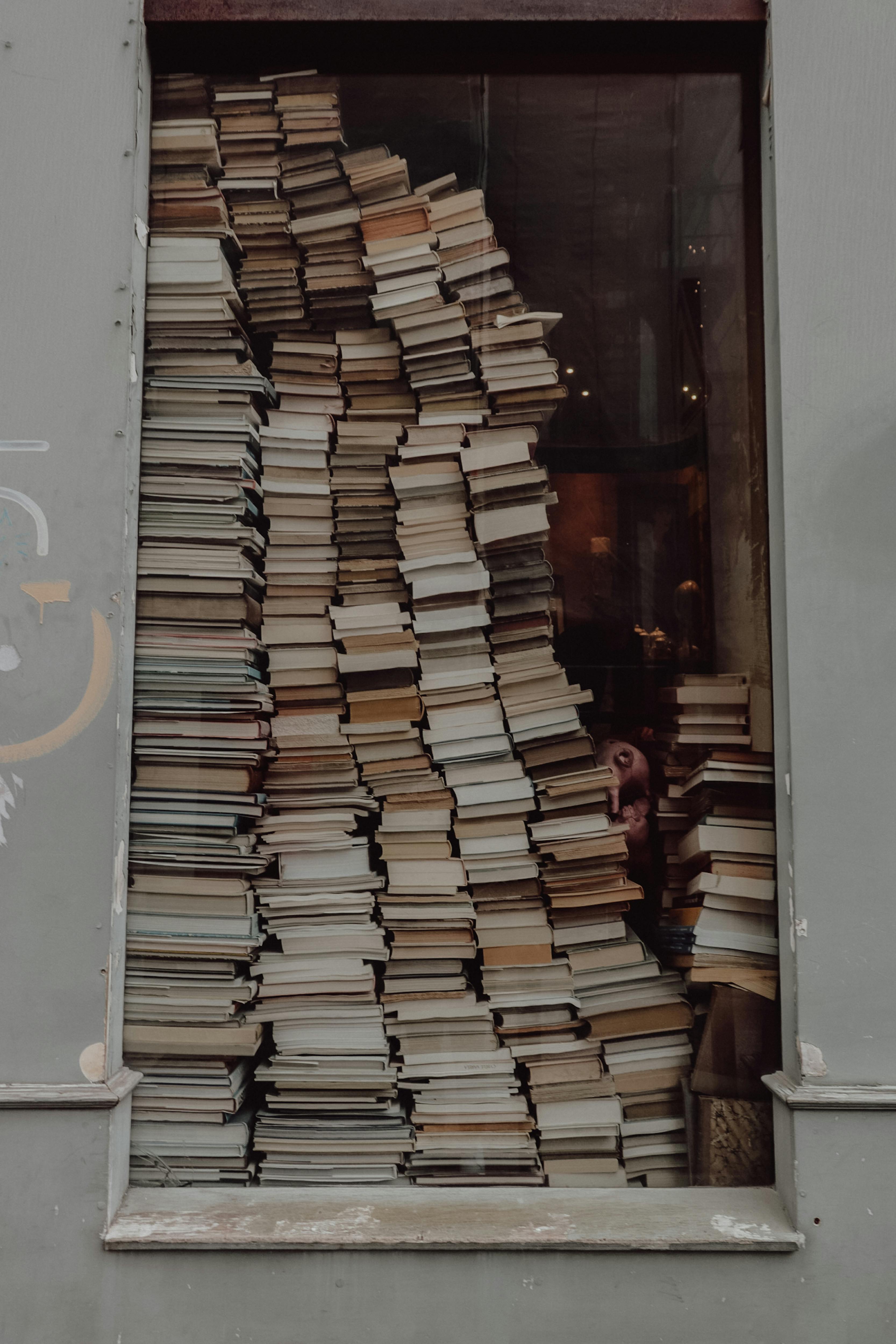 Vertical stacks of books fill a window, creating a vintage and artistic vibe.