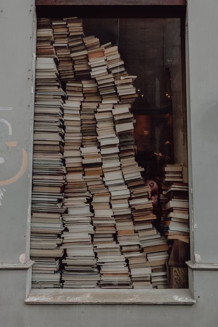 Vertical stacks of books fill a window, creating a vintage and artistic vibe.