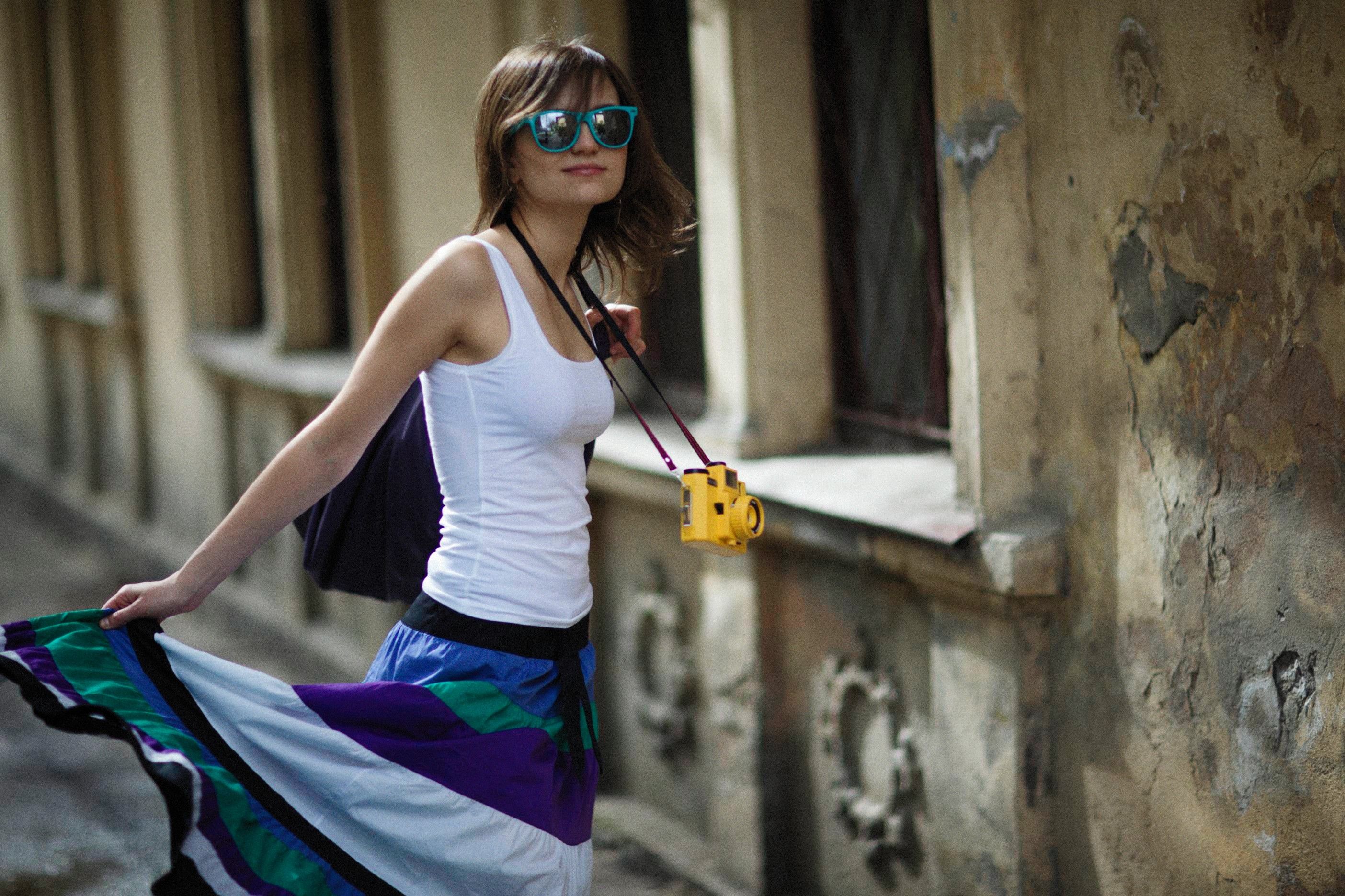 Trendy woman with sunglasses and camera walking by an old building.