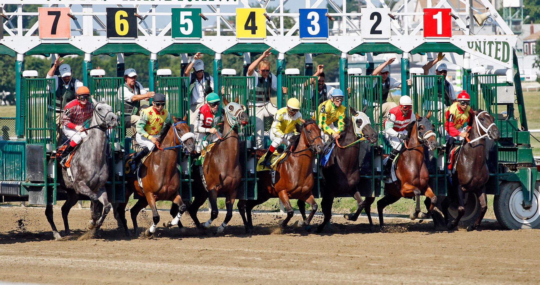 Horse race starting from the gate with jockeys in vibrant uniforms on a sunny day.