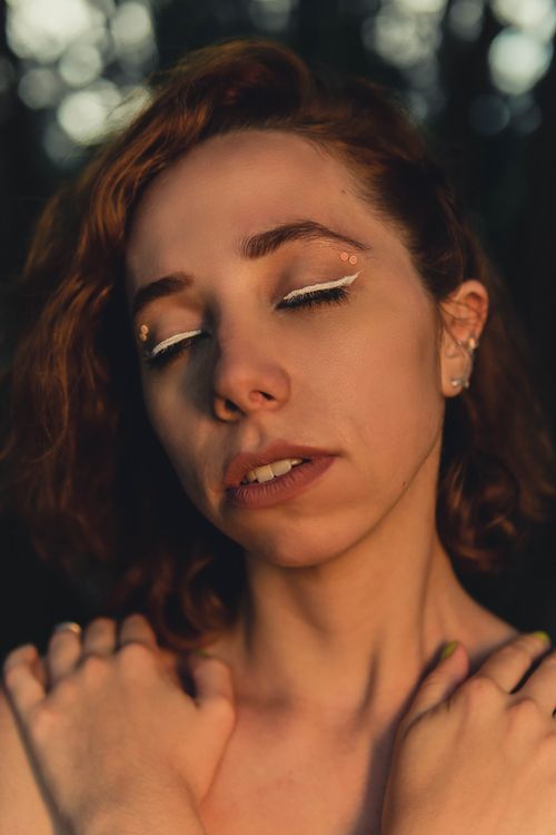 Free A close-up portrait of a woman with artistic eye makeup and closed eyes in a serene outdoor setting. Stock Photo