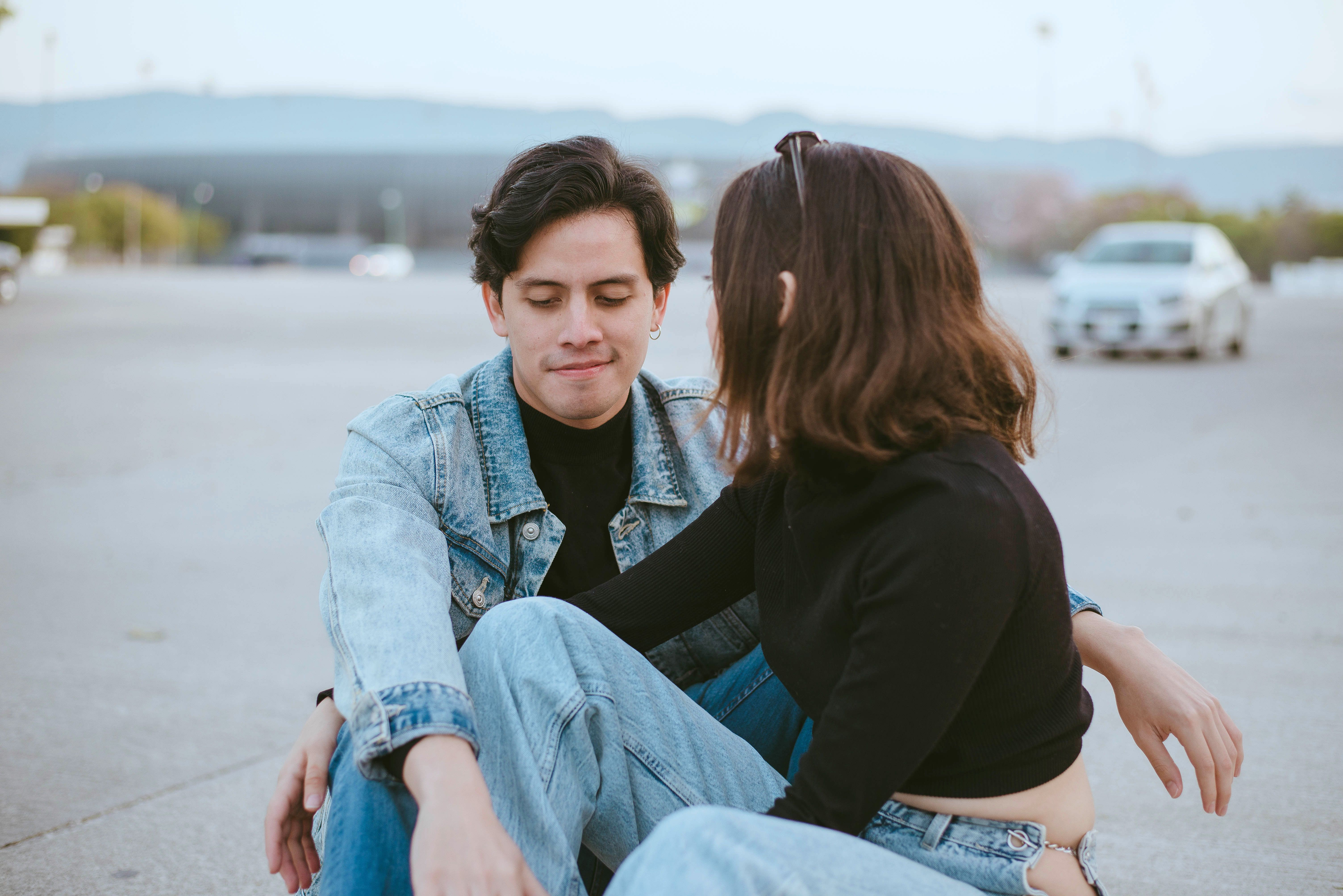 Young couple in casual denim outfits sitting together outdoors, embodying love and connection.