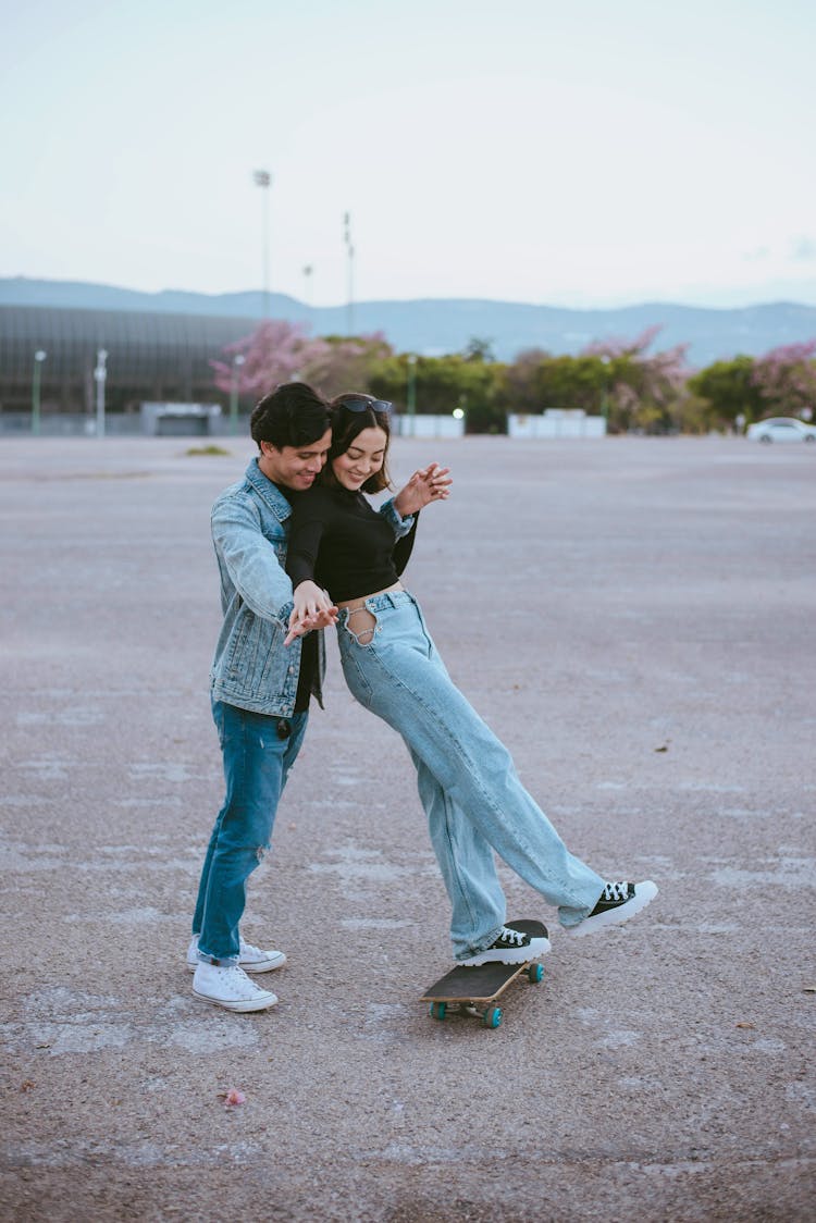 Teenage Boy Teaching Girl Skateboarding In Empty Parking Lot