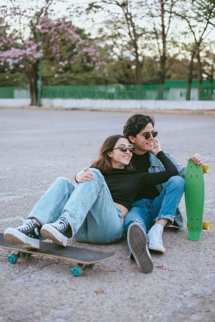 Happy teenage couple sitting on ground with skateboards at a park, enjoying leisure time.