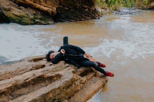Фотография человека, лежащего на камне у реки