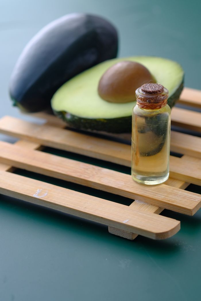Small glass bottle of avocado oil beside a halved avocado