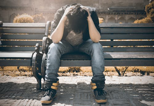 Uomo In Camicia Nera E Pantaloni Di Jeans Grigi Che Si Siede Sulla Panca Imbottita Grigia