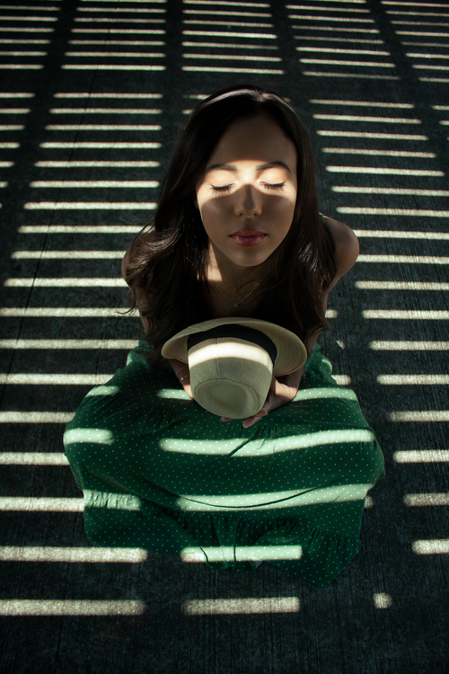 Free A young woman meditates with a fedora in sunlight casting striped shadows through patterns. Stock Photo