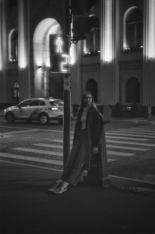 Free A young woman stands on a dimly lit street corner at night, embracing the city's monochrome ambiance. Stock Photo