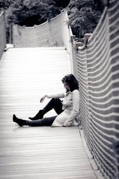 一位体贴的年轻女子身穿外套，坐在户外的木桥上