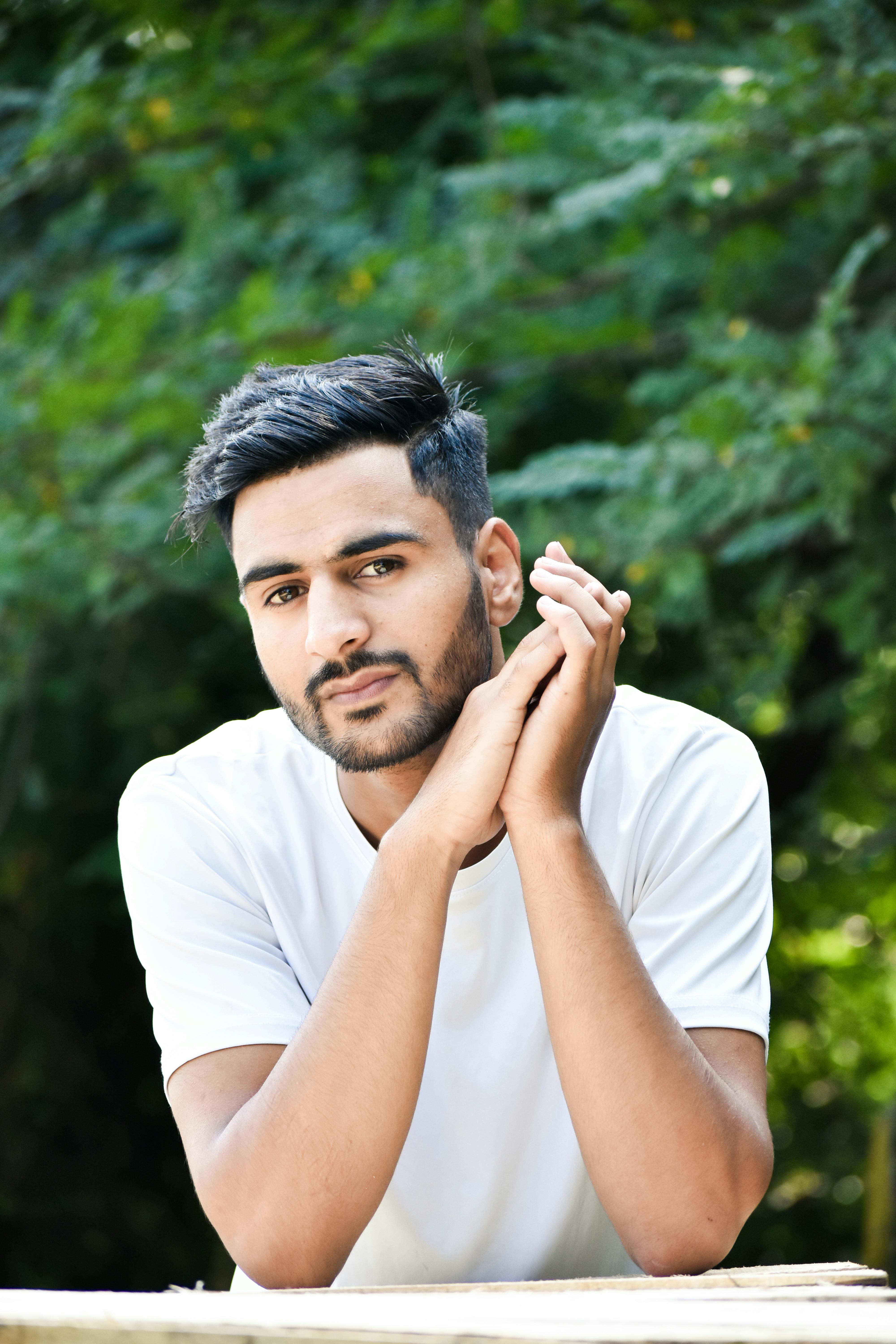 Handsome man in white t-shirt poses thoughtfully outdoors among greenery.