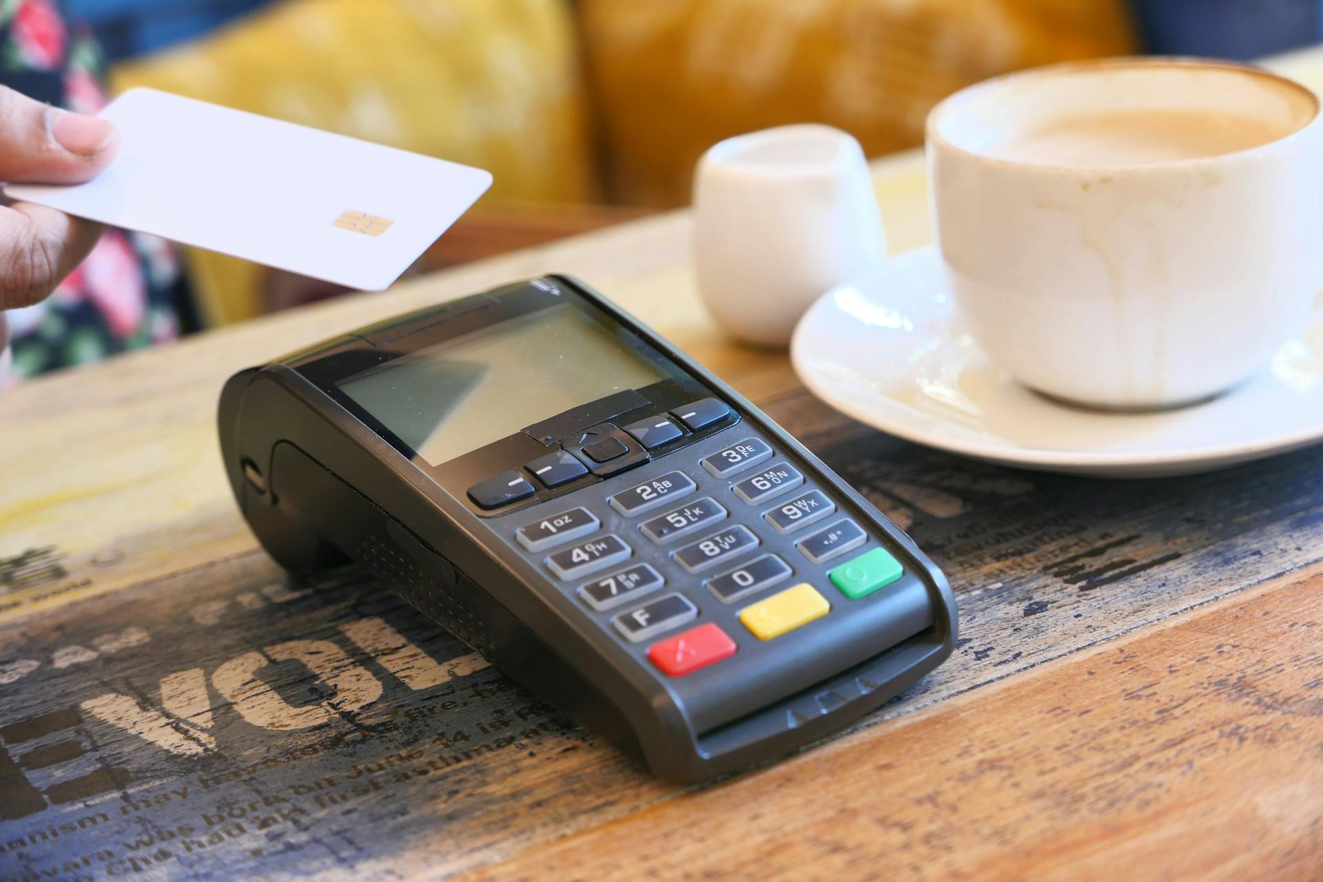 Close-up of contactless payment with credit card on a terminal beside a coffee cup.