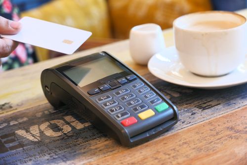 Free Close-up of contactless payment with credit card on a terminal beside a coffee cup. Stock Photo