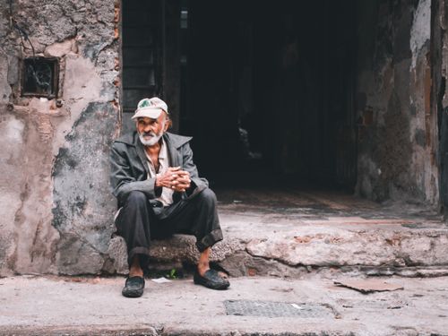 Free Portrait of an elderly man sitting thoughtfully on a rustic street corner, capturing urban life. Stock Photo