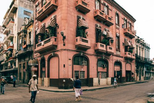 Free Charming pink building with balconies and people walking on an urban street corner. Stock Photo
