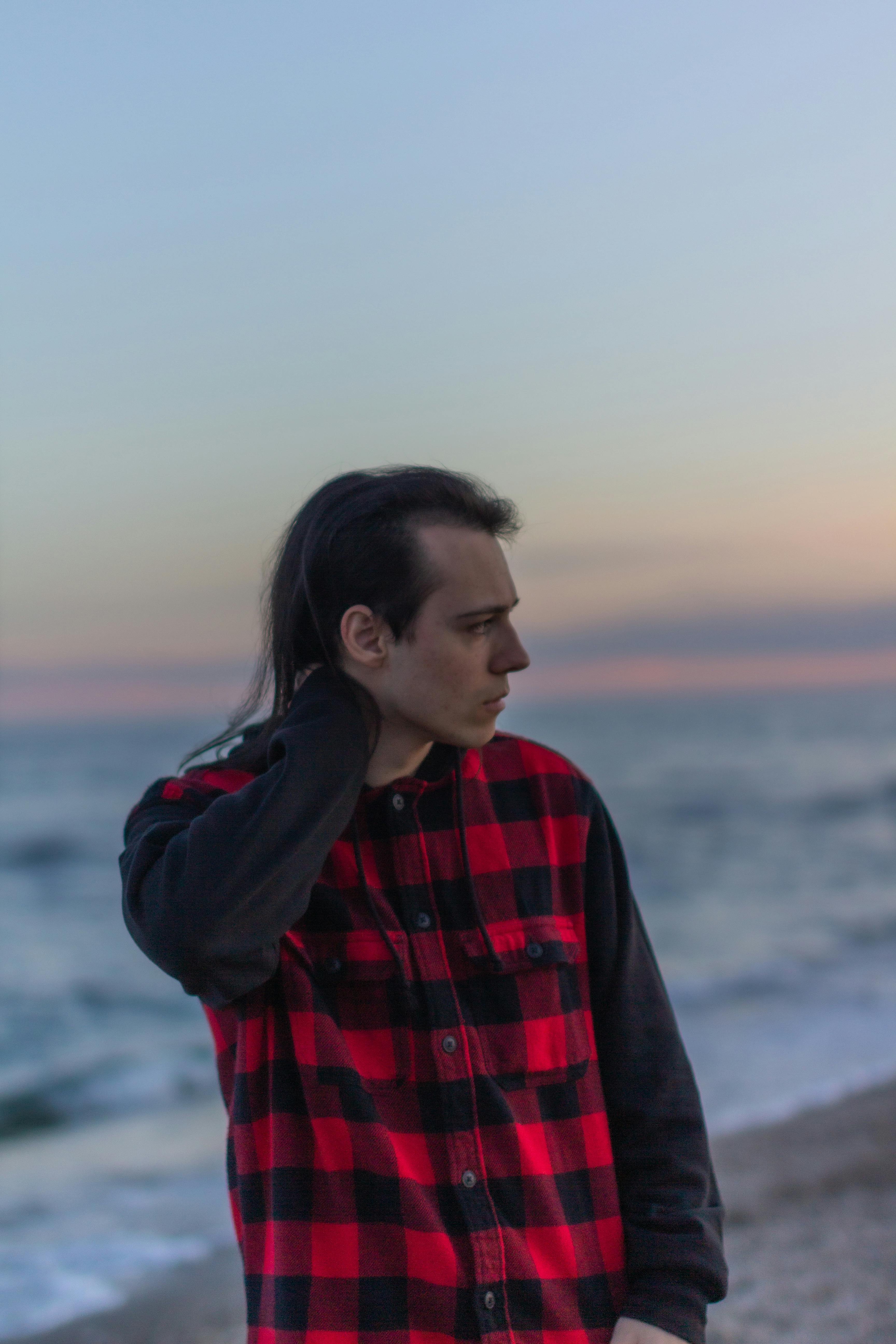 A Man in Checkered Jacket Standing on the Shore of a Beach while