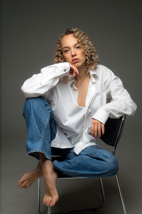 Young Woman with Blonde Curly Hair Posing in Studio Sitting on Chair 