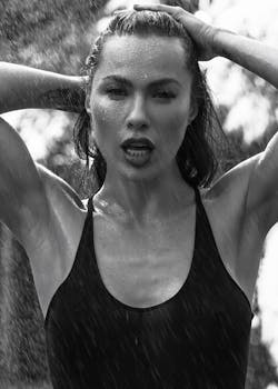 Candid black and white portrait of a woman in rain, hands on head.