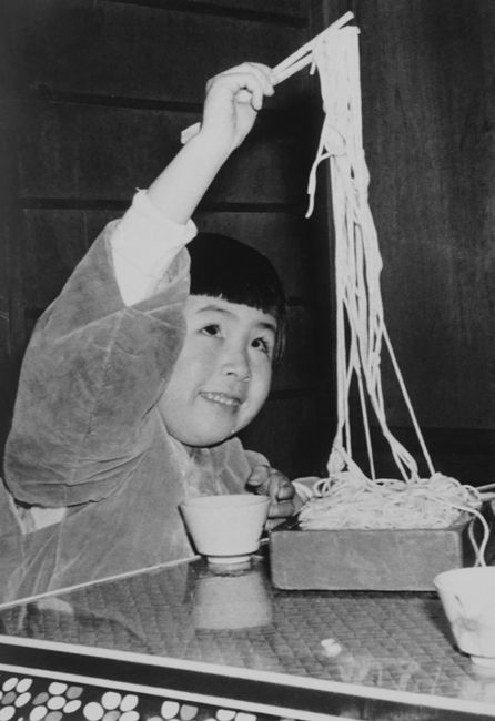 Monochrome image of a child eating noodles with chopsticks, capturing nostalgic Japanese culture.