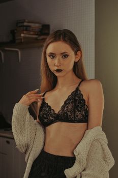 A young woman poses confidently in a black lace bralette and cozy sweater, exuding confidence.