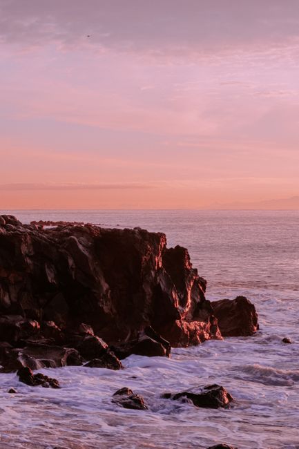Rugged cliffs by the sea under a pink sunset sky, creating a serene seascape view.