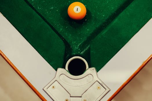 Orange billiard ball near pocket on a green pool table viewed from above. Perfect angle for gaming concept.