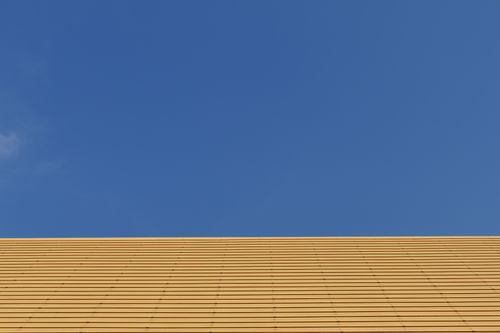 Free A minimalist architectural image featuring a yellow wall with a clear blue sky, emphasizing simplicity and contrast. Stock Photo