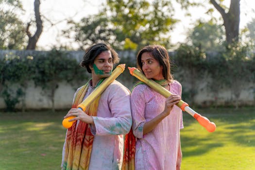 A joyful couple celebrating Holi with vibrant colors and water guns in a sunny outdoor setting.