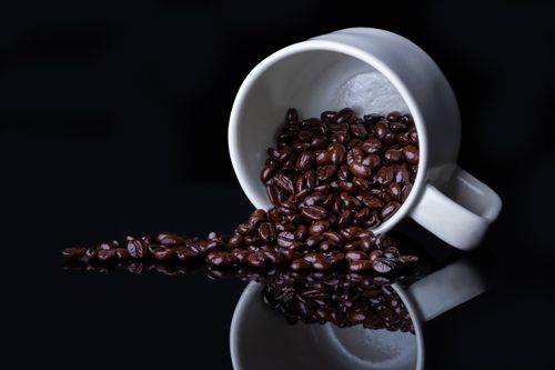 Free A cup tipped over with coffee beans spilling onto a glossy black surface. Stock Photo
