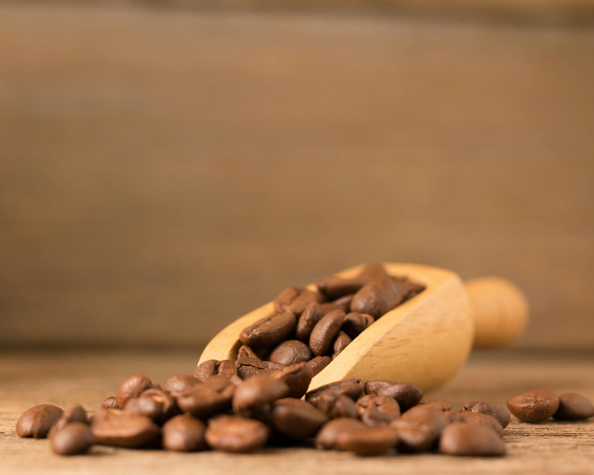 Close-up of roasted coffee beans with a wooden scooper on a wooden surface. Perfect for coffee themes.