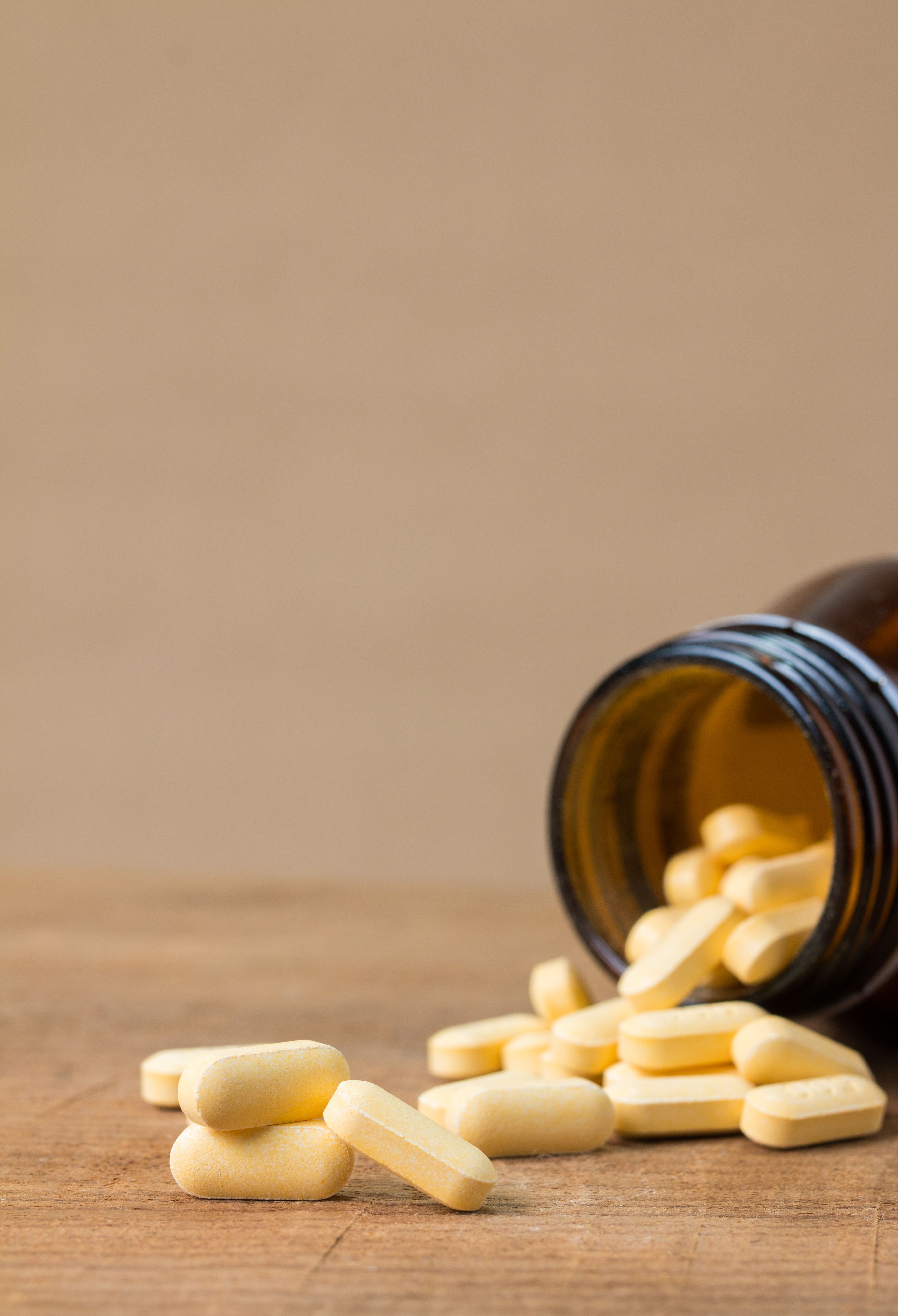 Horizontal view of yellow tablets spilling from a brown bottle on a wooden surface.