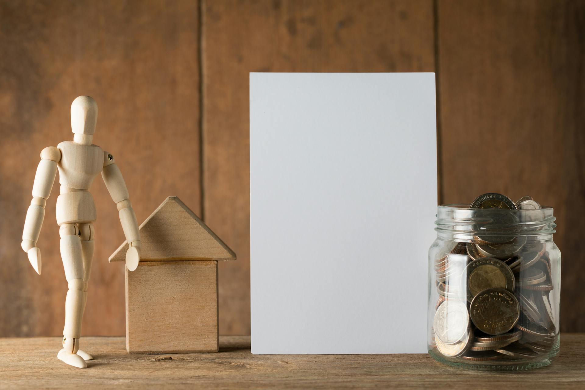 Wooden figure with jar of coins and blank card for financial planning or savings concept.