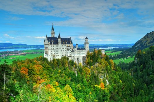 Aerial view of Neuschwanstein Castle amid vibrant autumn foliage with scenic landscape.