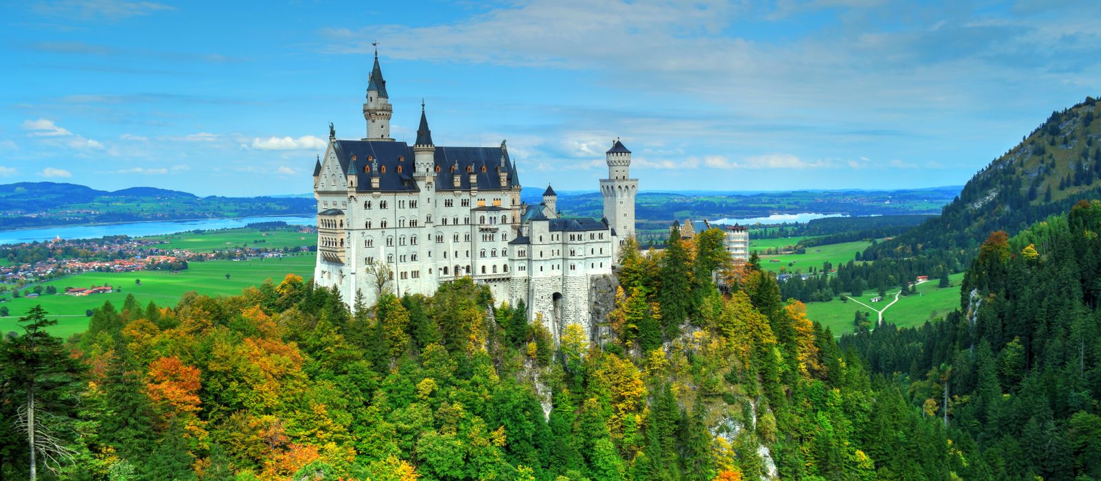Aerial view of Neuschwanstein Castle amid vibrant autumn foliage with scenic landscape.