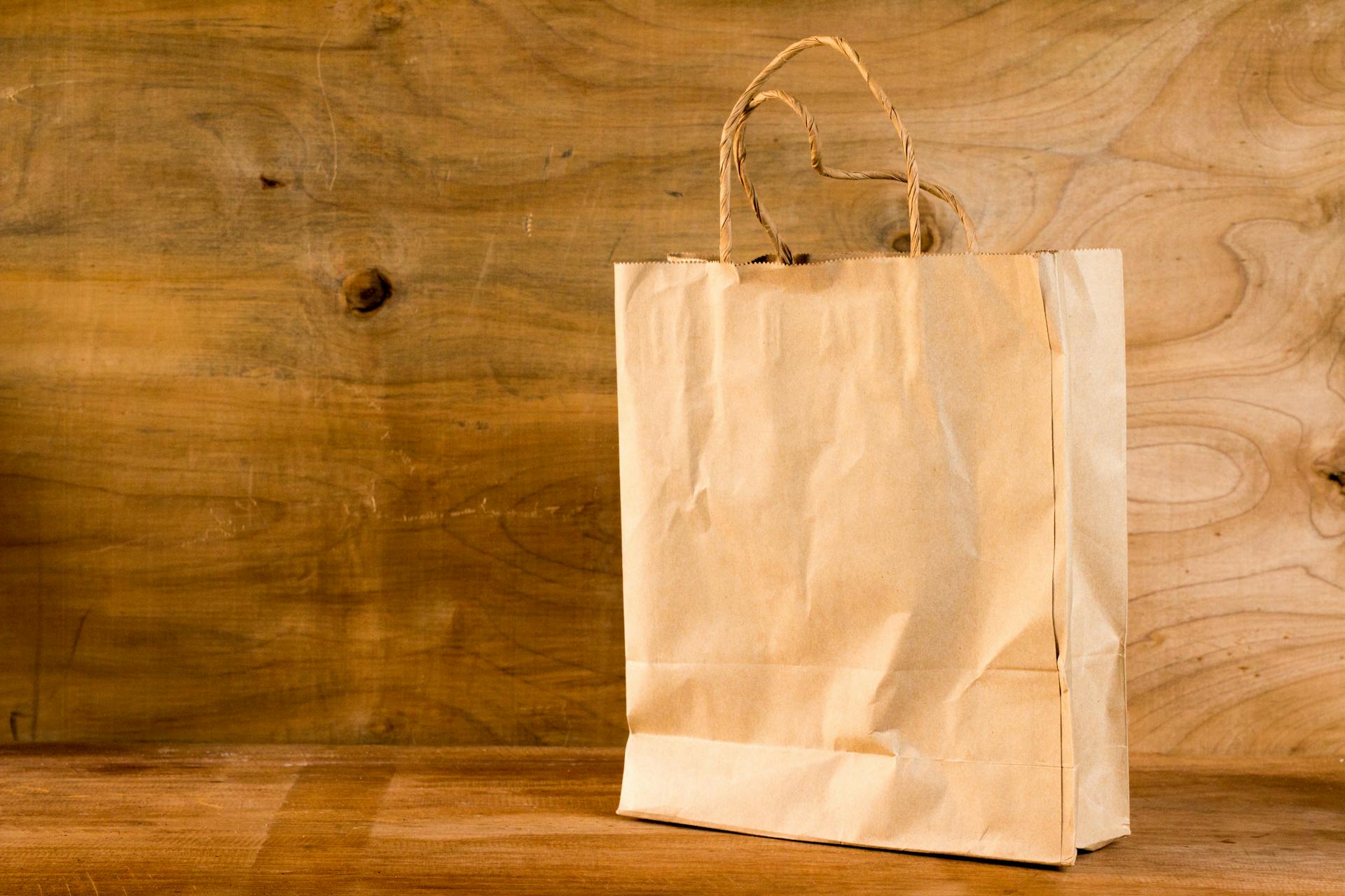 Close-up of a brown paper bag with handles on a wooden surface, offering warm earthy tones.
