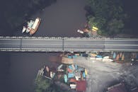 从空中俯瞰，一座河上的桥梁与穿行的船只、葱郁的绿植相映成趣，展现了自然与基础设施的和谐交融