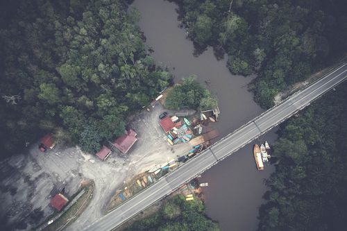 Free Aerial view of a bridge over a forested river with boats and road infrastructure. Stock Photo
