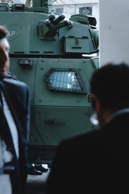 Green military vehicle showcased at an event, surrounded by observing individuals.